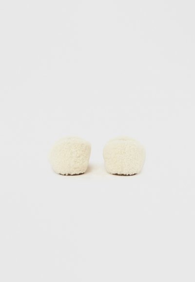 Paire de chaussons pelucheux de couleur crème avec des semelles brunes, placés côte à côte sur un fond blanc uni.