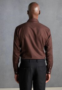 Bruin geruit overhemd met lange mouwen, knoopmanchetten en een rugpand, gecombineerd met zwarte op maat gemaakte broek. Glad textuur van de stof.