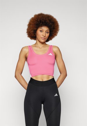 Rosa crop top med brede stropper, teksturert stoff og hvit Adidas-logo. Parret med høyt liv sorte leggings med hvite detaljer.