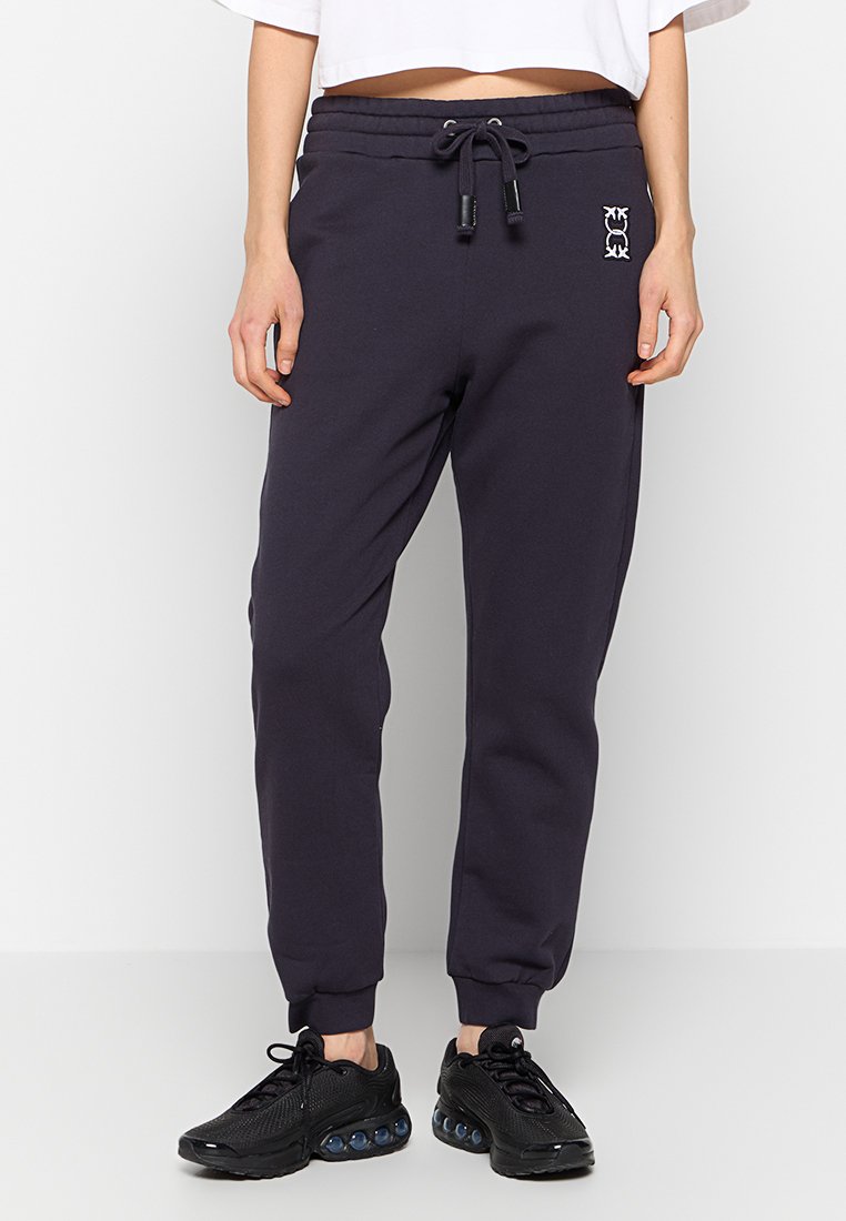 Granatowe spodnie dresowe wykonane z miękkiego materiału, z elastycznym paskiem w talii z sznurkiem, ściągaczami na nogawkach oraz małym logiem z przodu.