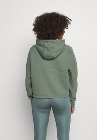 Felpa verde con finitura tessurizzata, vestibilità comoda e cappuccio attaccato, abbinata a leggings aderenti e lucenti di colore teal.