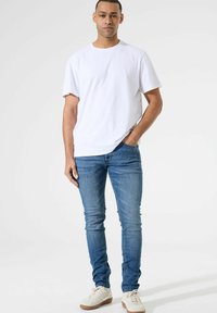 Witte katoen t-shirt, ontspannen pasvorm. Blauwe slim-fit jeans, denimstructuur. Witte sneakers met lichtbruine rubberen zolen. Geen opmerkelijke patronen of accenten.