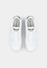 Hvite lær sneakers med rund tå, perforerte detaljer, flate lisser og en svart-hvitt merket tunge. Myk indre fôr.