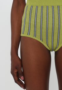 Visoko strukirane kratke hlače u svijetlozelenoj boji sa horizontalnim sjajnim prugama u plavoj i sivoj boji. Napravljen od teksturiranog, rastezljivog materijala.