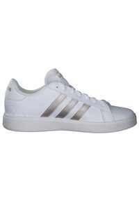 Baskets blanches avec trois rayures métalliques argentées, en matériau synthétique lisse et semelle en caoutchouc texturé. Présente un design à lacets.