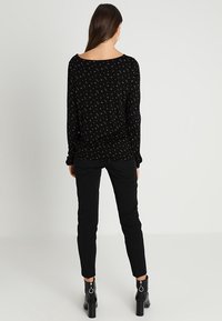 Schwarzes Langarmoberteil mit kleinen Blumenmustern, runder Ausschnitt und lockerer Passform, kombiniert mit schwarzen, figurbetonten Hosen und Stiefeletten mit Absatz.