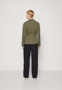 Olive green belted jacket with a smooth texture, featuring a collar and two side pockets, paired with black cargo pants and silver sneakers.