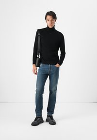 Suéter negro de cuello alto, diseño ajustado, combinado con jeans de mezclilla azul. Los accesorios incluyen un pequeño bolso cruzado negro y zapatillas deportivas negras.