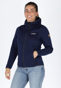 Giacca in pile blu navy con cappuccio, dotata di zip completa, tasche laterali e un logo sulla parte superiore del petto. Texture liscia e design aderente.