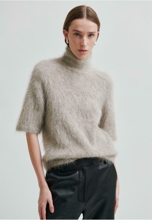 Ljusgrå, kortärmad polotröja med en fluffig textur, bärs över svarta läderbyxor. Tröjan har en avslappnad passform och en subtil lyster.