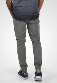 Grå avsmalnande byxor med elastiska muddar, tillverkade av ett lätt material. Kombineras med blå sneakers med en beige logotypdetalj.