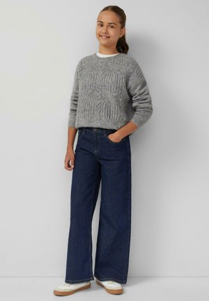 Grijze gebreide trui met een textuurpatroon, gecombineerd met wijde donkerblauwe denim jeans en witte sneakers met beige accenten.