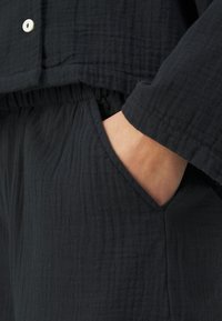 Schwarze, strukturierte Stoffkleidung mit einem lässigen Schnitt, Taschen und Knopfdetails sowie einem elastischen Bund.