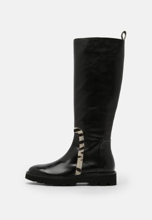 Czarna skórzana wysokie na kolano kozaki z masywną podeszwą, zaokrąglonym noskiem i paskiem w paski zebry po boku w okolicy kostki.