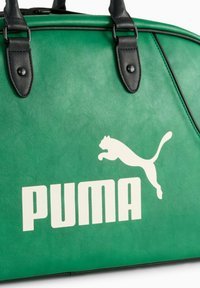 Zelena sintetička sportska torba s crnim kožnim detaljima, koja se ističe velikim bijelim logotipom "PUMA" i grafikonom puma koja skače.