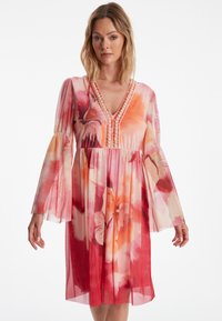 Blumenkleid mit V-Ausschnitt, durchsichtigen langen Ärmeln und rüschigem Saum. Es zeigt einen Farbverlauf von Rosa- und Rottönen mit gestickten Akzenten.