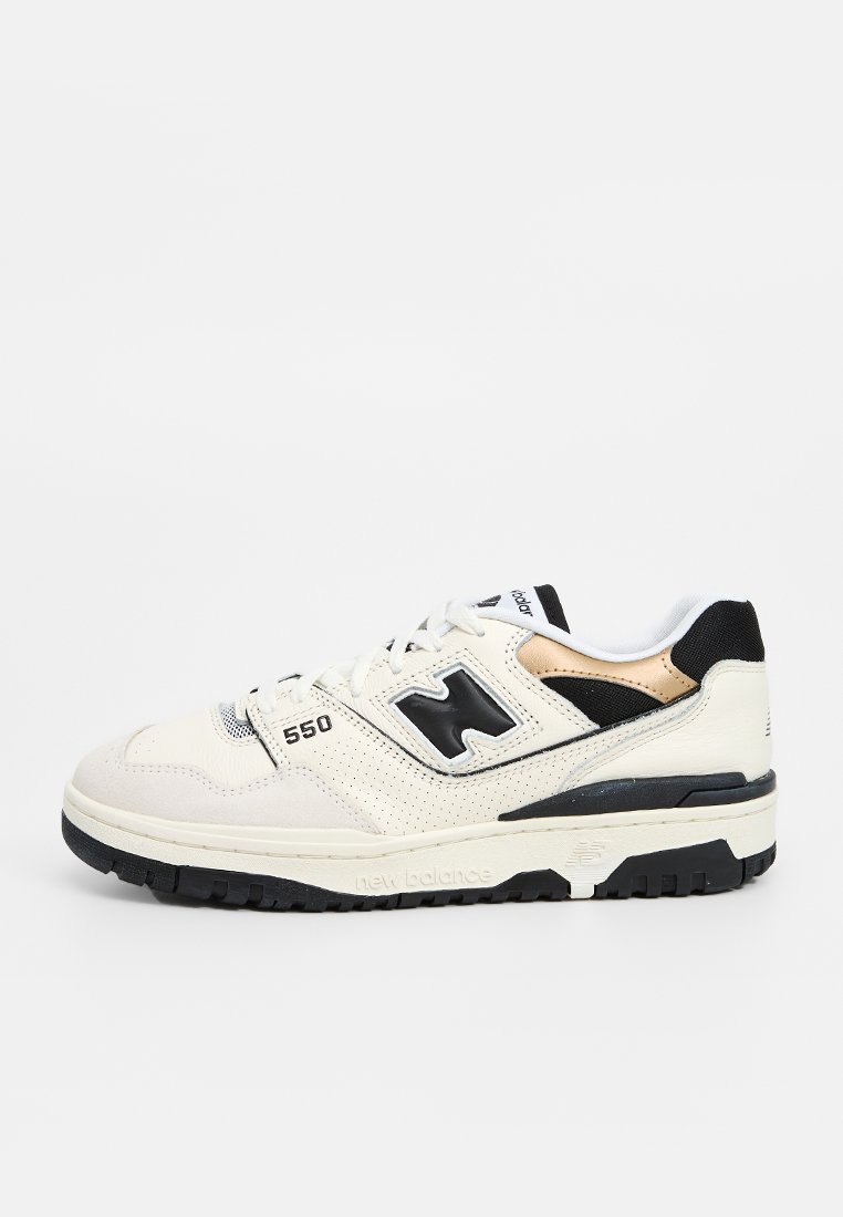 Weiße Ledersneaker mit schwarzen und goldenen Akzenten, perforierter Belüftung, dicker schwarzer Sohle und einem sichtbaren "550"-Logo an der Seite.