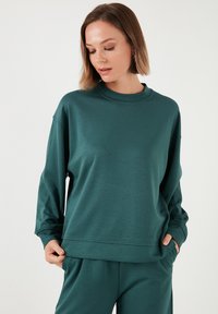 Felpa turchese con scollatura rotonda classica, maniche lunghe e vestibilità comoda. Texture morbida e liscia con dettagli cuciti e tasche laterali.