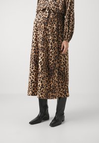 Hame leopard print, pehmeästä kankaasta, polven pituinen, solmimisvyötäröyksityiskohdalla, yhdistettynä polven korkeisiin mustiin nahkabootseihin. Rakennepinta.