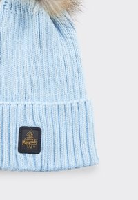 Berretto lavorato a maglia di un azzurro chiaro con texture a coste. Presenta un pom-pom in finta pelliccia e una patch rettangolare nera con un logo dorato.