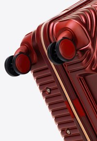 Red hard-shell suitcase with textured surface, zip closure, two black wheels, and metallic accents for durability and mobility.