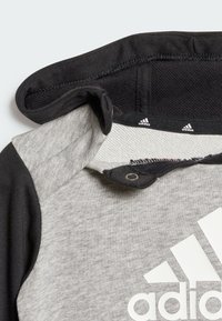Felpa grigia con cappuccio nero, caratterizzata da un logo Adidas bianco. Presenta un tessuto testurizzato e un collo sicuro con chiusura a pressione.