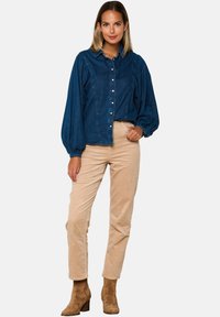 Denim bluza v temno modri barvi z naborki in zapiranjem na gumb, v kombinaciji s bež kord pantami in svetlorjavimi čevlji z visokim peto.