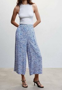 Housut, joissa on leveät lahkeet ja vaaleansininen sekä valkoinen kukallinen paisley-kuosi, varustettuna joustavalla vyötärökillä ja kevyellä kankaalla. Yhdistettynä istuvaan valkoiseen toppiin.