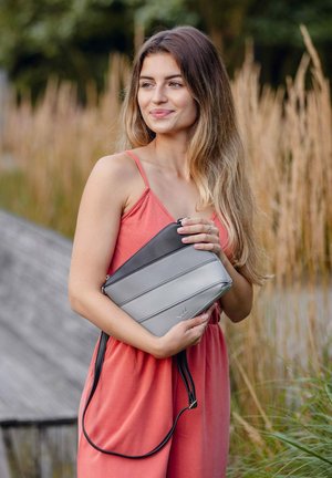 Šedá a černá křížová taška s vodorovnými pruhy, vyrobená z hladkého materiálu. Obsahuje zip a nastavitelné rameno.