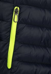 Marine pufferjakke med svart glidelås og lys gul glidelåsbånd, med quilted tekstur og glatt, glanset finish.