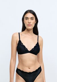 Bralette noir avec des bordures en dentelle, de forme triangulaire et doté de bretelles réglables, associé à un sous-vêtement noir avec des accents en dentelle assortis.
