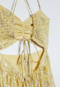 Haut court smocké jaune à fines bretelles, avec une fermeture à nouer à l'avant et un motif floral. Tissu doux et léger avec une coupe décontractée.