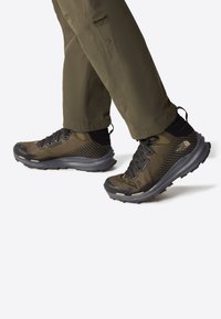 Brown and black athletic shoes with mesh fabric and rubber soles; features laces, a rear pull tab, and textured patterns on sides.