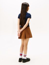 Top corto navy a maniche corte, gonna plissettata marrone, calze bianche fino al ginocchio con strisce rosse e navy, e scarpe nere. I capelli sono lunghi e lisci.