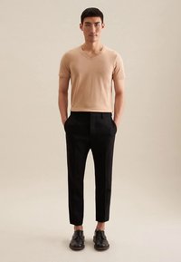 Maglione a maniche corte con scollo a V abbinato a pantaloni sartoriali neri. L'outfit presenta un design aderente e una texture liscia. Scarpe nere completano il look.