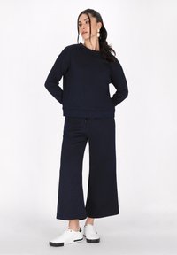 Completo loungewear blu navy composto da un maglione testurizzato con scollo rotondo e pantaloni a gamba larga, abbinato a sneakers bianche.