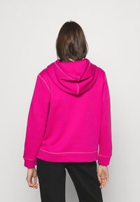 Fuchsiová mikina s kapucí a stahovací šňůrkou, žebrovanými manžetami a spodním lemem. Měkká textura s kontrastními švy. Pohled zezadu bez vzoru.