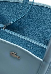 Interno di una borsa a tracolla in pelle azzurro chiaro, caratterizzato da una tasca con zip, finitura texturizzata e un piccolo logo in rilievo. Cinghie lisce con dettagli in metallo.
