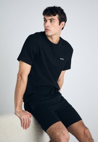 Tricou negru cu mânecă scurtă, cu o textură ribbată, având un mic logo "BOSS". Asortat cu pantaloni scurți negri, ambele având un design minimalist.
