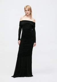 Robe noire décolletée avec des manches longues, présentant une coupe ajustée et une texture froncée sur l'ensemble. Jupe évasée en bas.