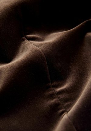 Brun sammetstyg med en slät yta, med mjuka veck och sömmar. Ytan verkar rik och glänsande med en lätt lyster.
