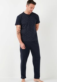 Conjunto de pijama en color navy que incluye una camiseta de manga corta con un patrón de diamantes y tres botones, combinada con pantalones largos a juego. Tejido suave, ajuste relajado.
