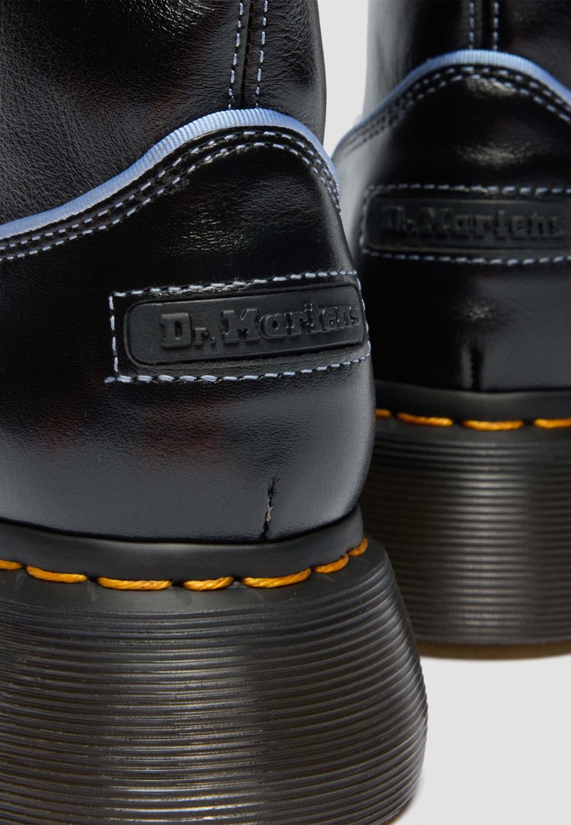 Black leather Dr. Martens boots featuring yellow stitching, thick ribbed soles, and embossed logo patches on the back heels.