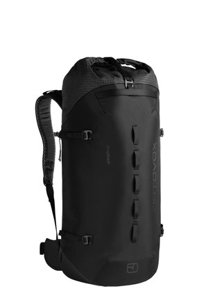 Mann trägt ein graues T-Shirt, hellbraune Hose, Wanderschuhe und einen großen schwarzen Wanderrucksack, steht vor einem einfarbigen Hintergrund.