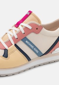 Baskets de sport en mélange de matériaux : mesh beige, accents en cuir rose et bleu, lacets blancs et détail en métal réfléchissant sur le talon.