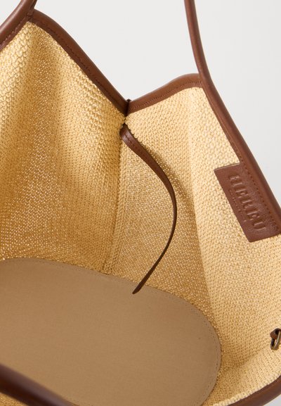 Vue intérieure d'un sac fourre-tout tissé beige ouvert avec une garniture en cuir marron, une petite étiquette en cuir et une sangle en cuir marron à l'intérieur.