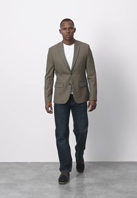 Zielony oliwkowy blezer o dopasowanym kroju, zestawiony z białym t-shirtem, ciemnoniebieskimi dżinsami i brązowymi butami na sznurówki. Gładka tekstura i klasyczny design.