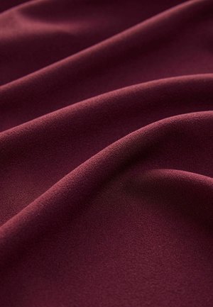 Bordeauxfärgad tyg med en slät, matt yta, draperad i mjuka, flödande veck som visar en enhetlig färg och subtil djup.