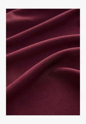 Burgundi szövet, sima, matt textúrával, puha, folyó redőkben, melyek egységes színt és finom mélységet mutatnak.