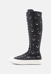 Botas de caneira alta pretas com atacadores em pele texturizada, apresentando detalhes em metal prateado e ilhós circulares, com uma sola em borracha branca.